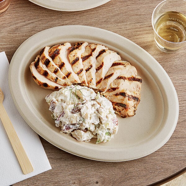 A World Centric oval compostable fiber plate with food on it on a table.