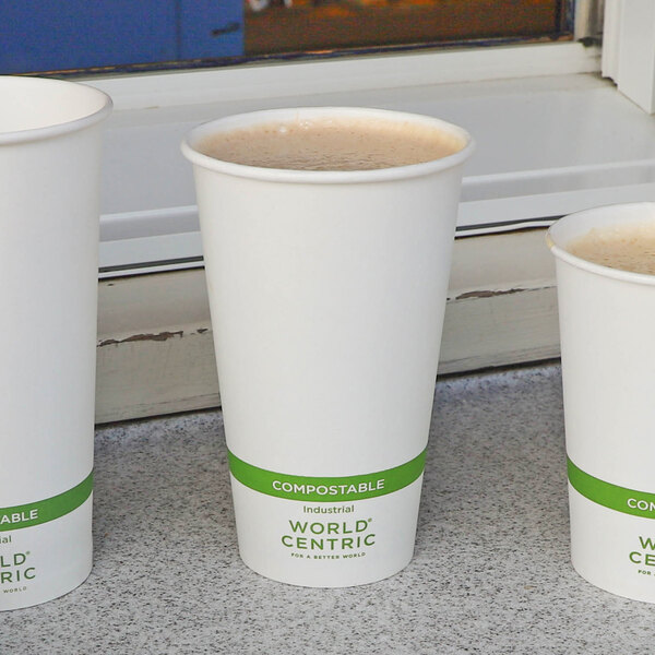 A white paper cup filled with a hot beverage, featuring a green band labeled 'COMPOSTABLE' and 'WORLD CENTRIC' near the bottom.