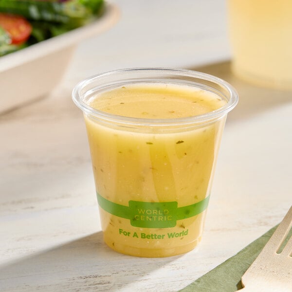 A clear 3 oz. compostable portion cup filled with yellow salad dressing.