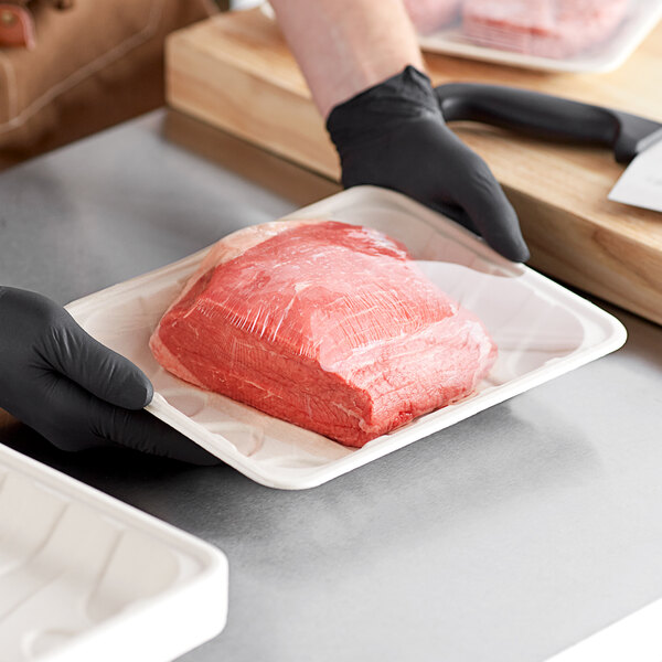 A person in black gloves holding a World Centric compostable fiber meat tray filled with meat.