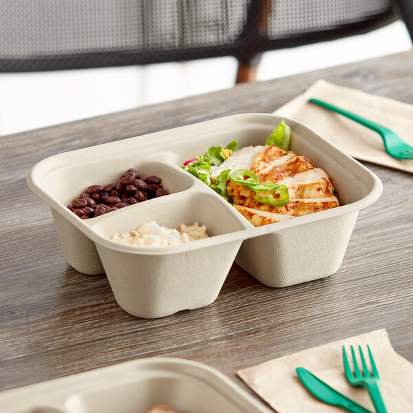 A World Centric compostable fiber container with three compartments filled with food on a table.