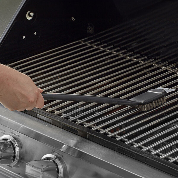 A person using a Mr. Bar-B-Q Deluxe Grill Brush to clean a barbecue grill grate.