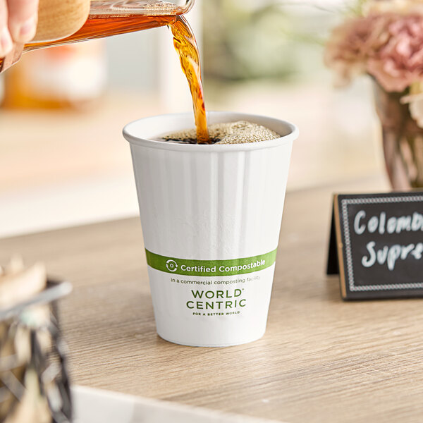 A person pouring brown liquid into a World Centric white paper hot cup.