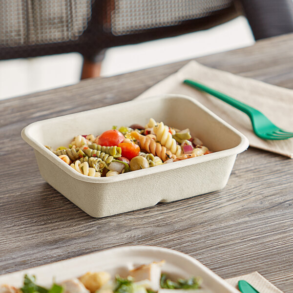 A World Centric compostable fiber container filled with pasta and vegetables with a green plastic fork on a napkin.