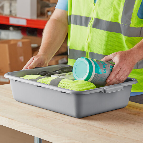 A person in a reflective vest putting food in a gray Lavex utility bin.