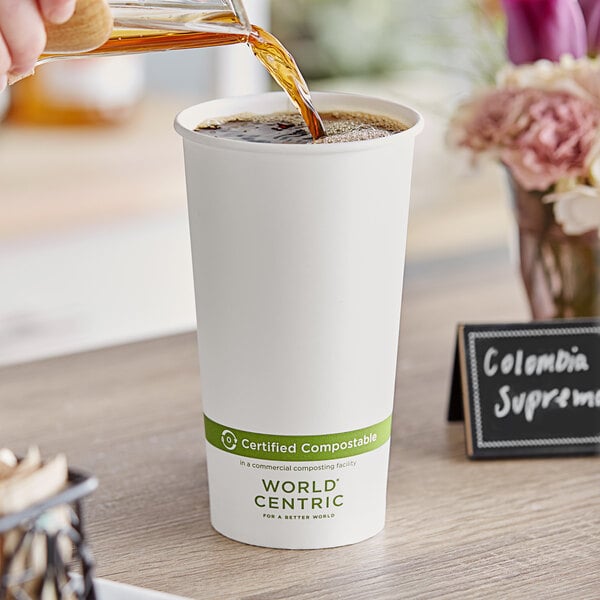 A person pouring coffee into a World Centric white compostable paper hot cup.