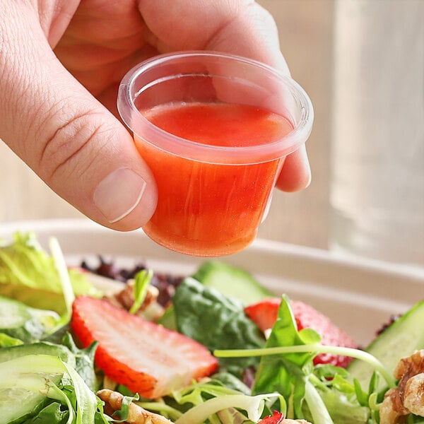 A hand holding a World Centric compostable PLA portion cup of red liquid.