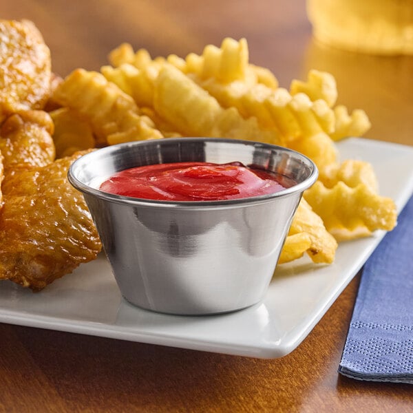 A table with a bowl of ketchup next to a plate of chicken wings and fries.