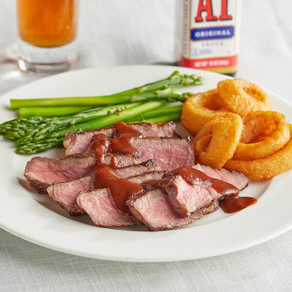 A plate of steak and asparagus with a white and red container of A.1. Steak Sauce on the table.