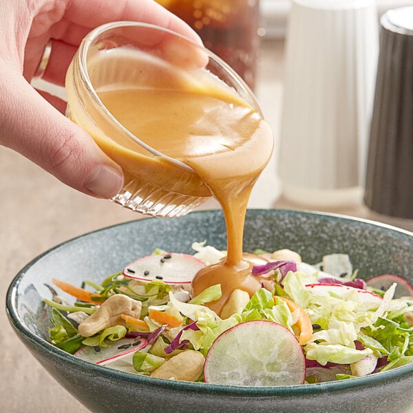 A hand pouring Kraft Signature Oriental Sesame Dressing into a bowl of salad.