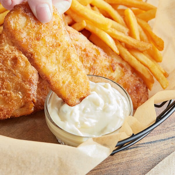 A person dipping a fried fish finger into a bowl of white sauce.