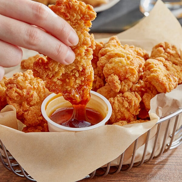 A hand dipping a piece of fried chicken into a Mike's Hot Honey dip cup.