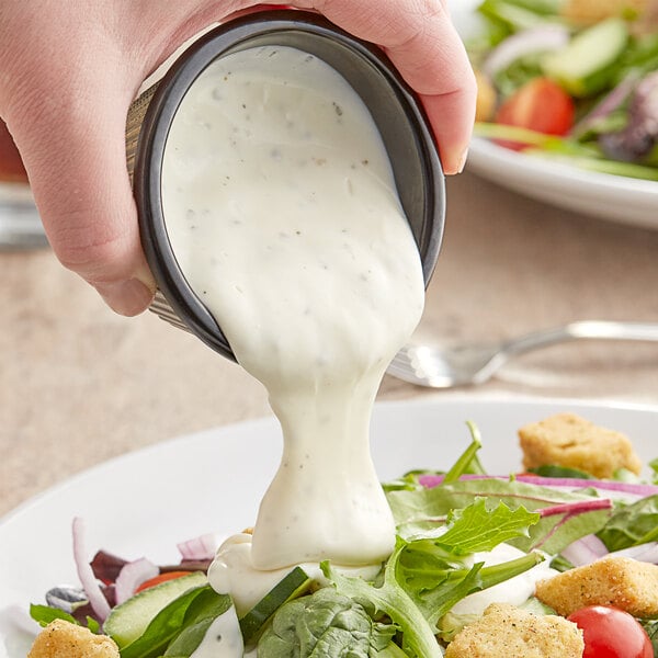 A person pouring Kraft Ranch dressing onto a salad at a salad bar.