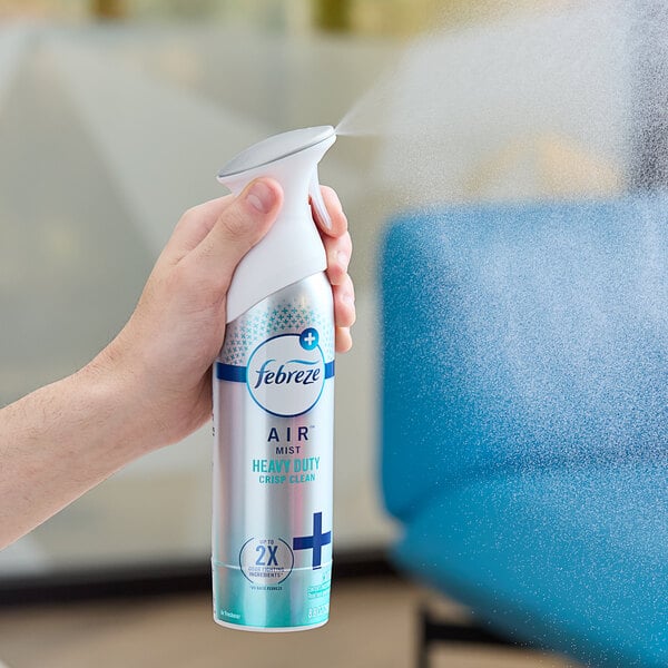 A person using Febreze Air Heavy-Duty Crisp Clean scented air freshener spray in a white room.