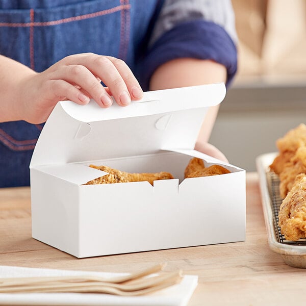 A person holding a white Choice take out lunch box filled with chicken wings.