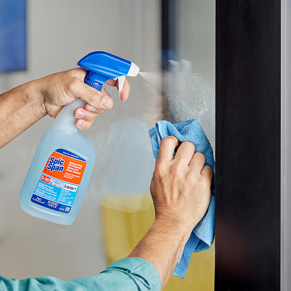 A hand using Spic and Span Disinfecting All-Purpose and Glass Cleaner to spray a window.