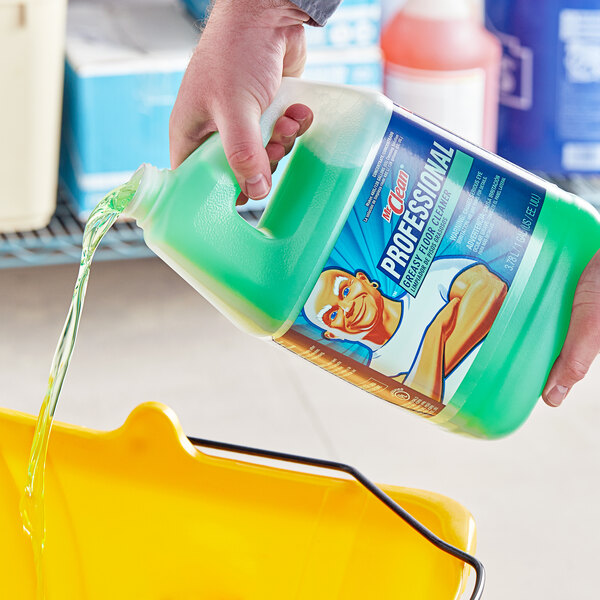 A hand pouring Mr. Clean Professional Greasy Floor Cleaner from a yellow bottle into a bucket.