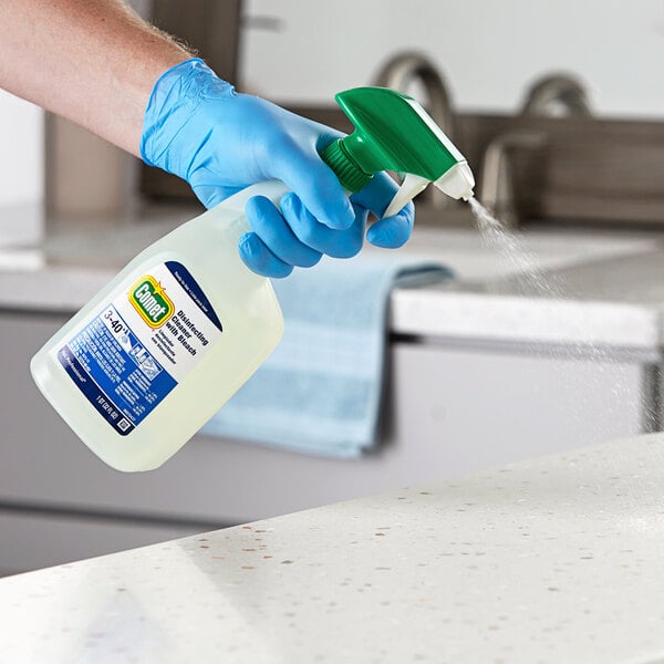 A hand in a blue glove spraying Comet all purpose cleaner on a counter.