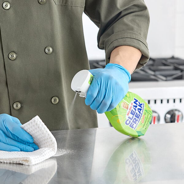 A person wearing blue gloves spraying Mr. Clean All-Purpose Cleaner on a counter.