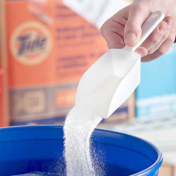 A hand pouring Tide Professional white powder into a blue container.