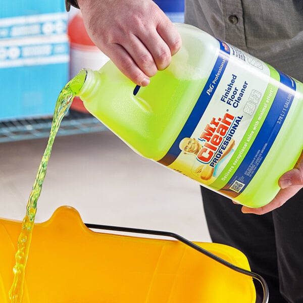 A hand pouring Mr. Clean Professional Concentrated Finished Floor Cleaner into a yellow bucket.