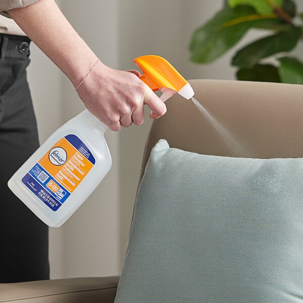 A person holding a white Febreze spray bottle and spraying a chair.