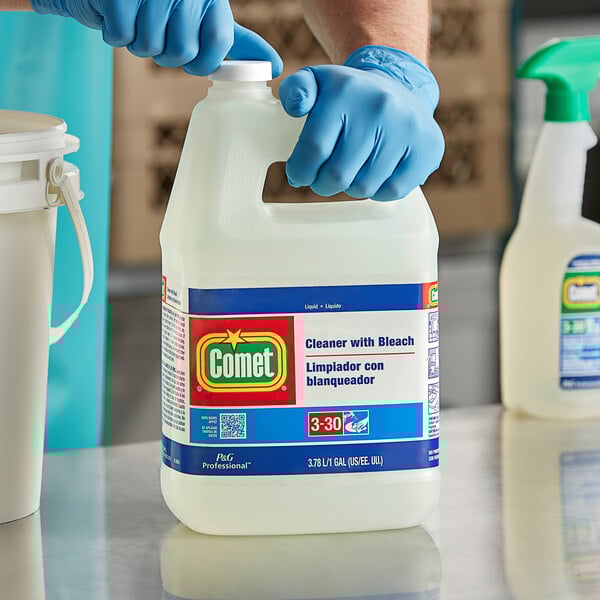 A person in blue gloves holding a white jug of Comet bleach cleaner.