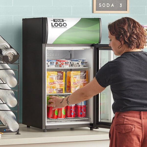 A woman opening the swing door of an Avantco countertop display refrigerator.