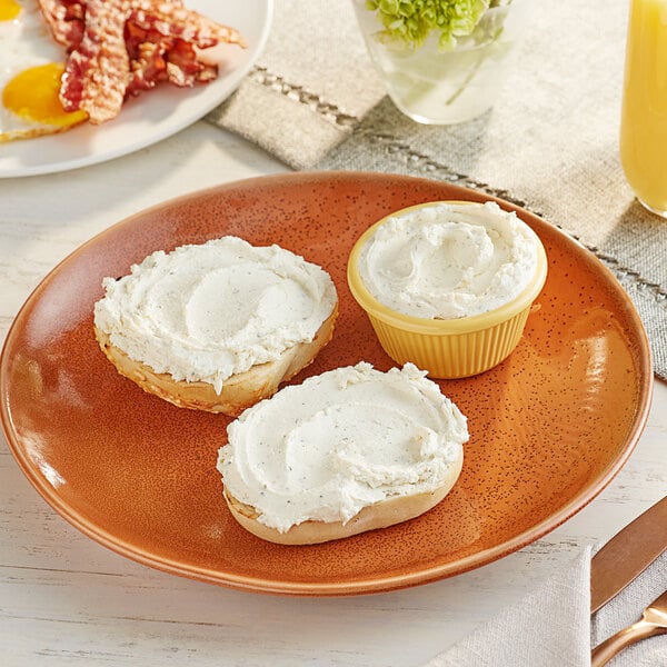 A plate of food with a bagel and eggs with a bowl of garlic and herbs cream cheese on a wood table.