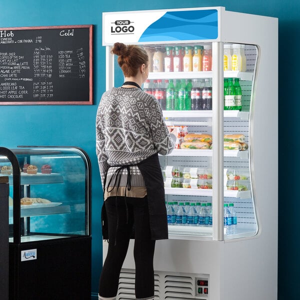 An Avantco white refrigerated air curtain merchandiser with a woman looking at food on shelves.