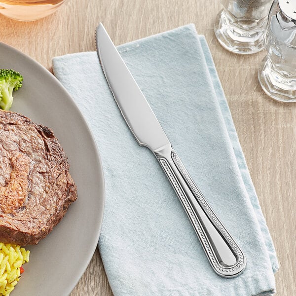 An Acopa stainless steel steak knife on a napkin next to a plate of food.