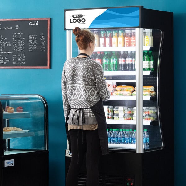 A woman standing in front of a black Avantco refrigerated air curtain display case.