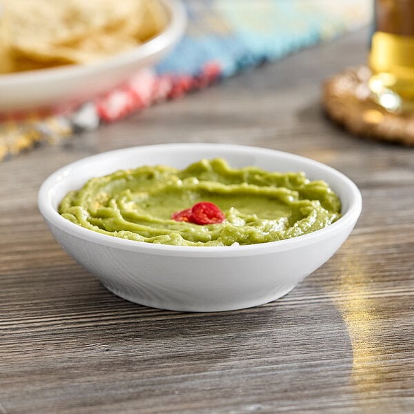 An American Metalcraft white mini melamine bowl of guacamole with chips on a table.