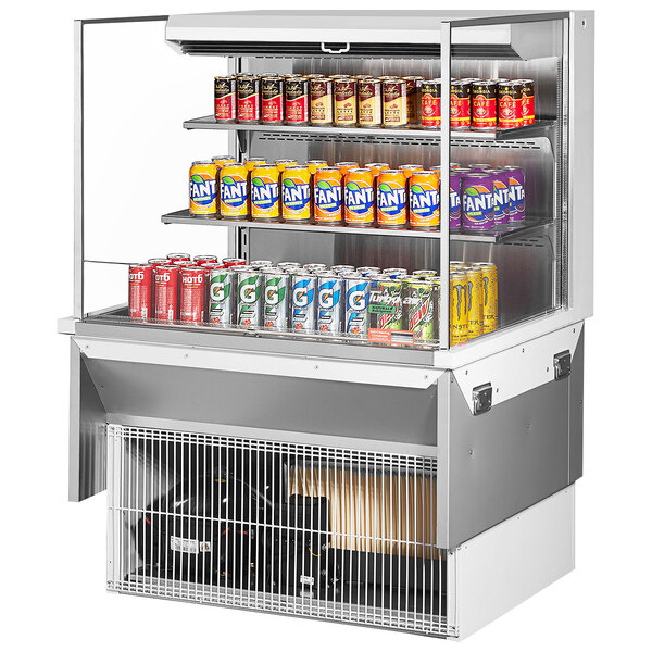 A Turbo Air white drop-in refrigerated open display case with cans of soda and beer on shelves.