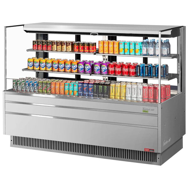 A Turbo Air stainless steel horizontal refrigerated curtain merchandiser filled with cans of soda on shelves.