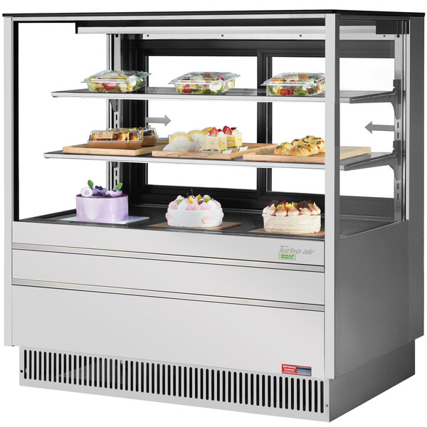 A Turbo Air stainless steel refrigerated bakery display case with flat glass shelves holding cakes and desserts.