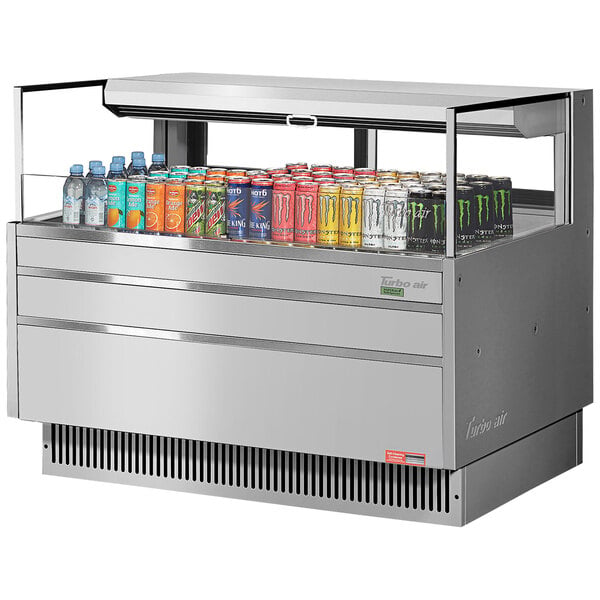 A Turbo Air stainless steel horizontal refrigerated merchandiser with cans of soda and different colored drinks inside.