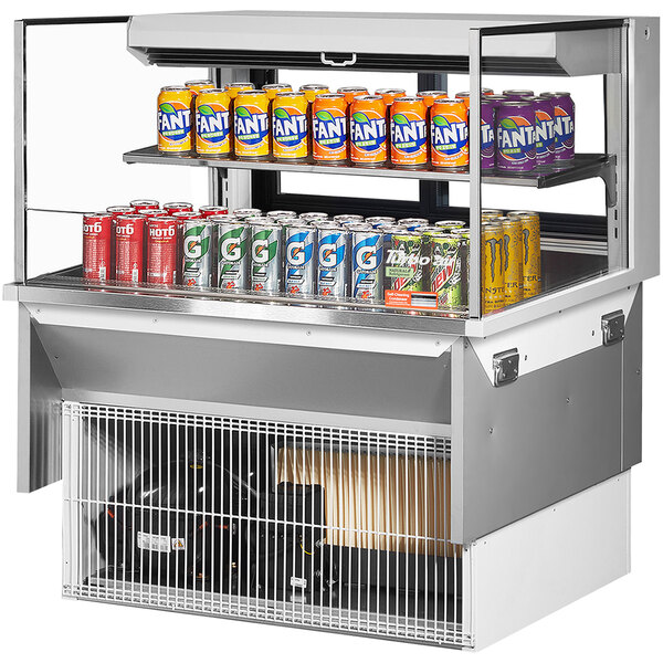 A Turbo Air white drop-in refrigerated open display case with cans of soda on a shelf.
