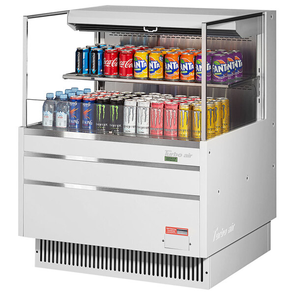 A white Turbo Air horizontal refrigerated curtain cooler with cans on a shelf.