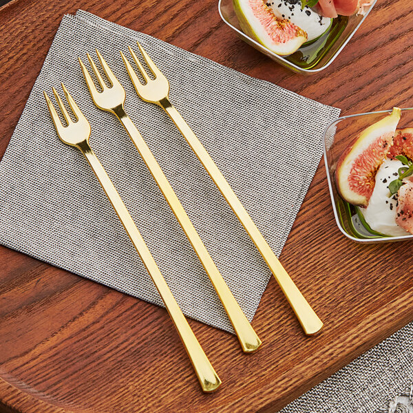 A pair of Visions gold plastic tasting forks on a table next to a bowl of fruit.