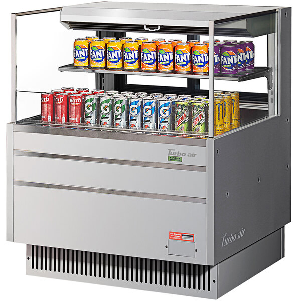 A Turbo Air horizontal refrigerated curtain merchandiser with cans of soda on a shelf.