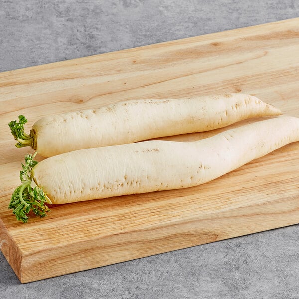 Two Fresh Daikon Radishes on a wooden cutting board.