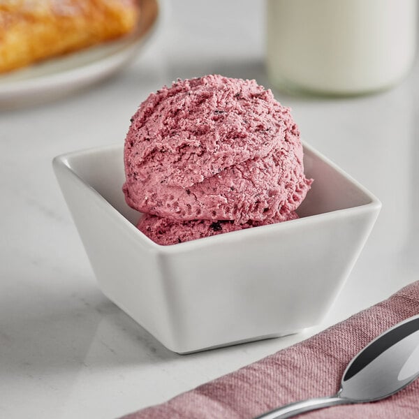 A bowl of blueberry ice cream with a spoon on a cloth.