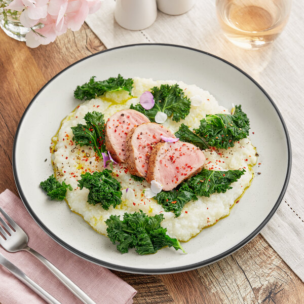 An Acopa Embers grey matte coupe stoneware plate with pork and kale on it.