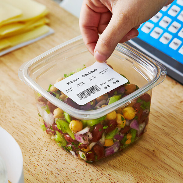 A hand using an AvaWeigh white blank label to mark a plastic container of food.