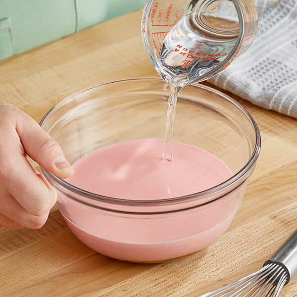 A hand pouring Oringer Citric Acid into a bowl of pink liquid.