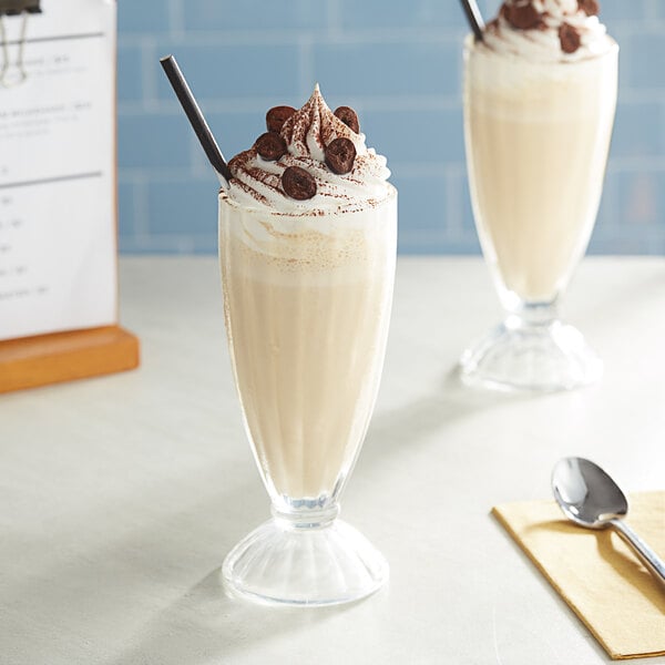 A glass of Oringer coffee milkshake with whipped cream and chocolate chips on a table next to a spoon.