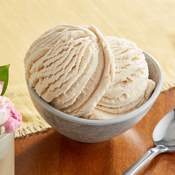 A bowl of Oringer pistachio hard serve ice cream with a spoon on a table with flowers.