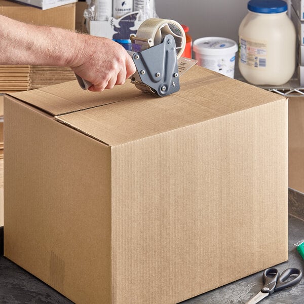 A hand using a box cutter to open a Kraft shipping box.