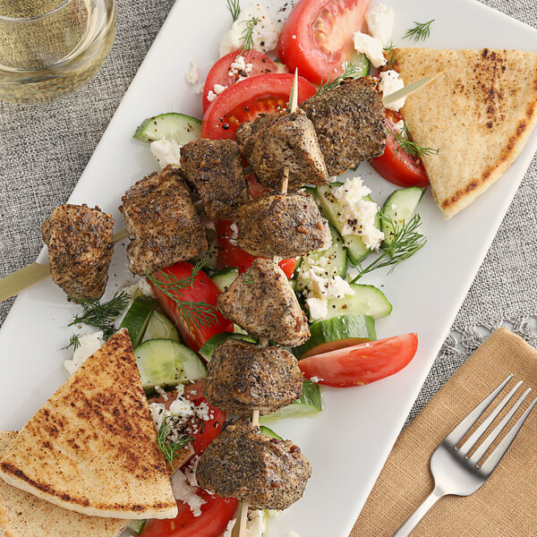 A plate of food with a piece of meat on a skewer and bread with McCormick Culinary Greek Seasoning on a table.